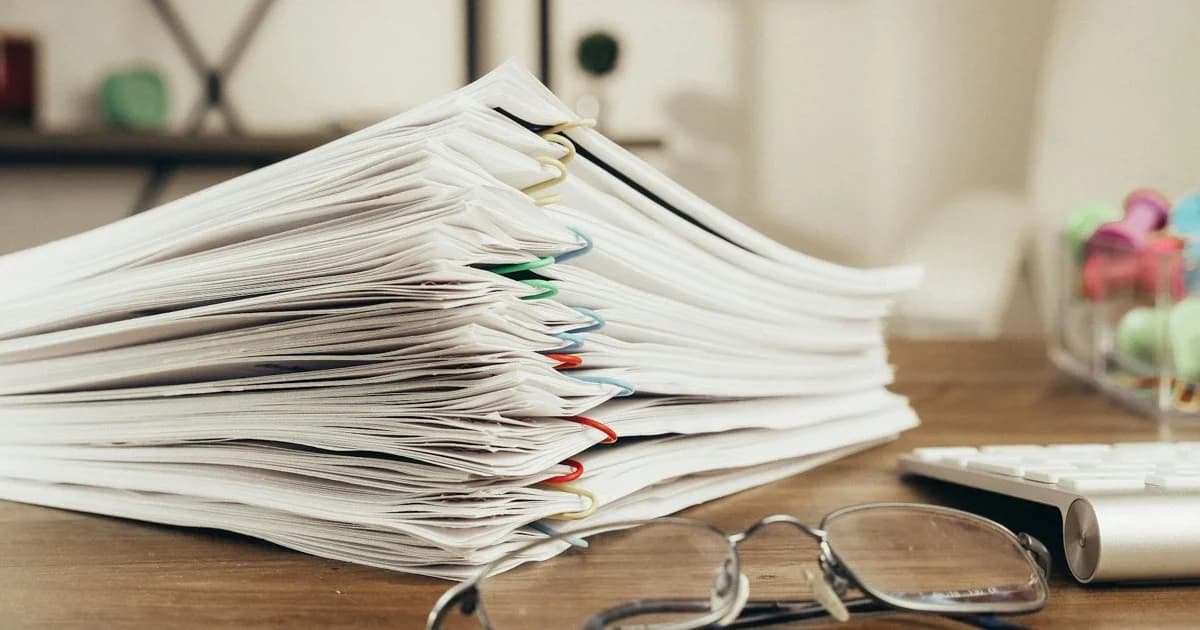 Stack di documenti ordinati su scrivania con occhiali, tema automazione documentale aziendale