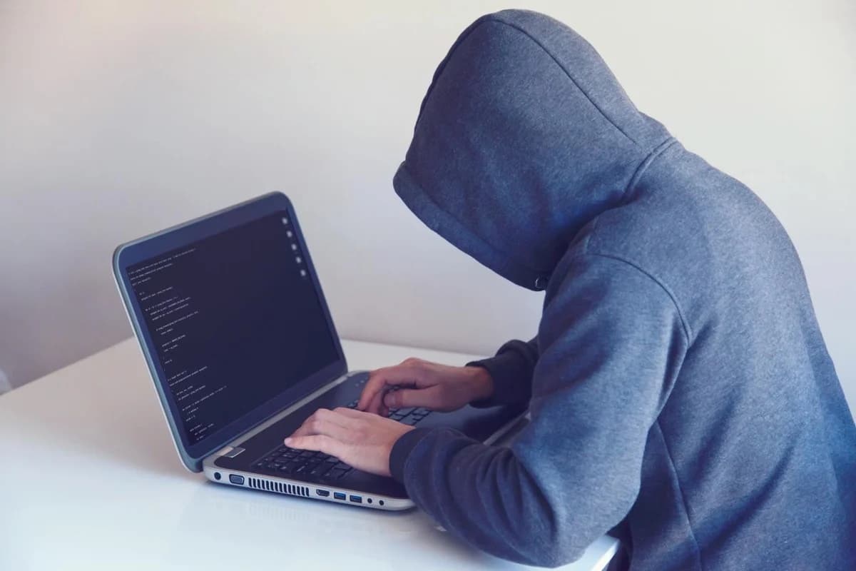 Figura anonima in felpa che lavora al computer, rappresentazione di un attacco informatico